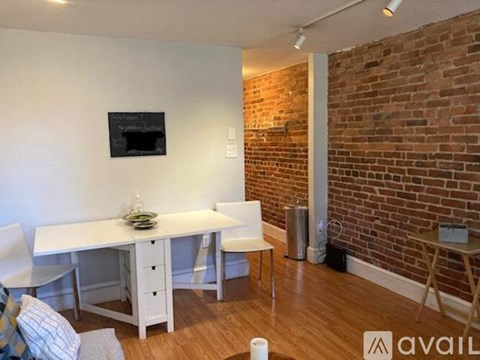 A living room with a grey couch, a white dining table and a red rug.