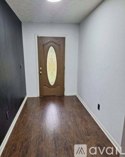 A wooden door with a glass window is in the middle of a hallway with dark wood flooring and white walls.