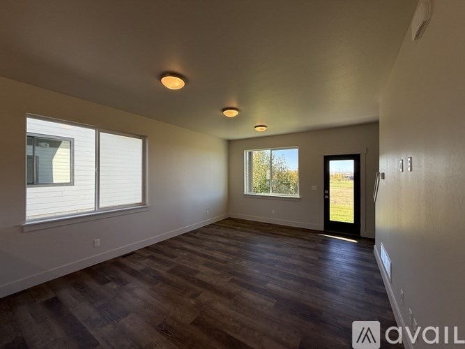 A spacious room with wooden flooring and a view of trees through a window.