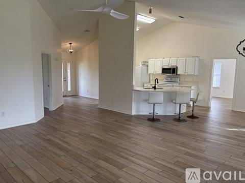 A living room with a kitchen in the background and a dining table with chairs in the foreground.