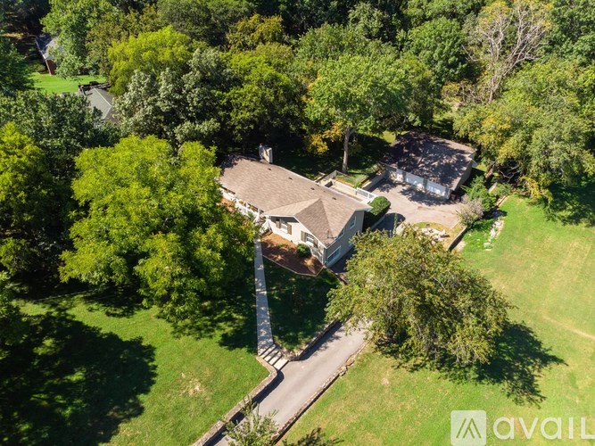A house surrounded by trees with a driveway leading to the front door.