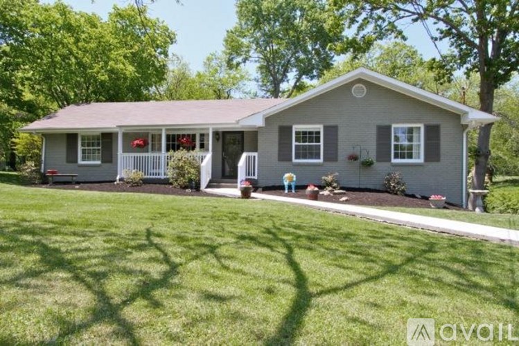 A house with a grey roof and white trim is surrounded by green grass and trees.