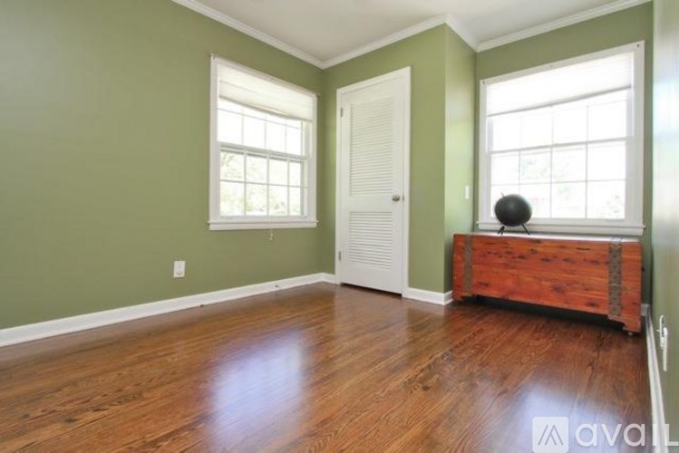 A room with green walls and wooden floors, with a white door and two windows.