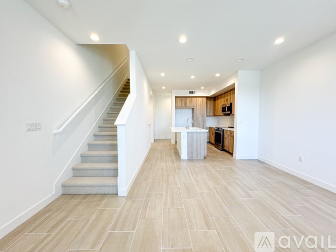 A spacious, well-lit room with a staircase and a kitchen area.