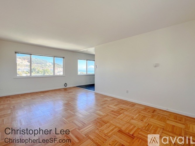 A room with wooden flooring and two windows overlooking a landscape.