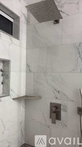 A shower area with a marble wall and a shower head.