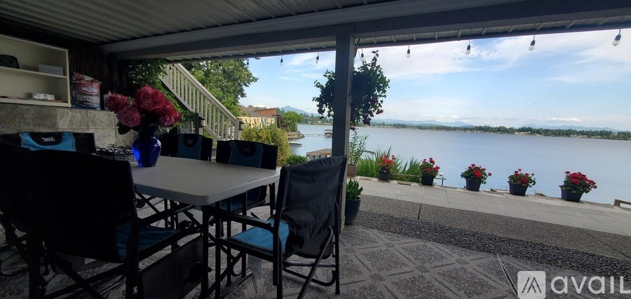 A table with chairs and a vase of flowers is set up on a patio overlooking a lake.