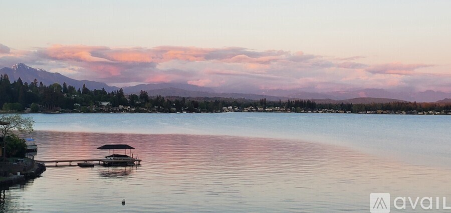 A serene lake with a boat and a dock in the foreground and mountains in the distance.