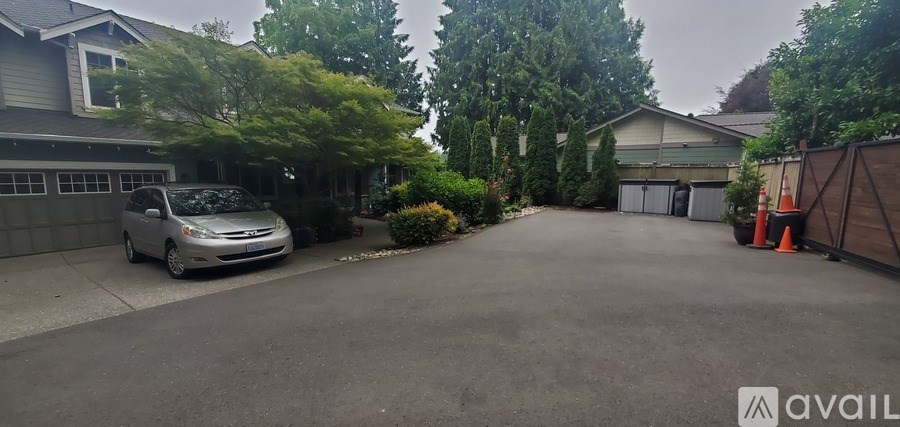 A grey car is parked in a driveway with a house and trees in the background.