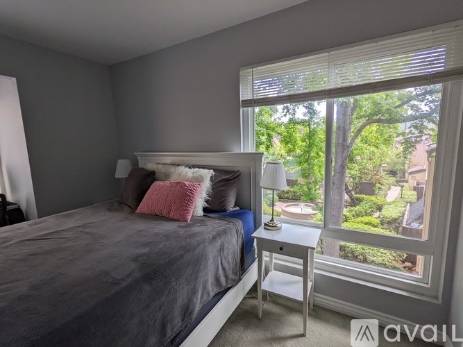 A bedroom with a bed, nightstand, and window overlooking a garden.