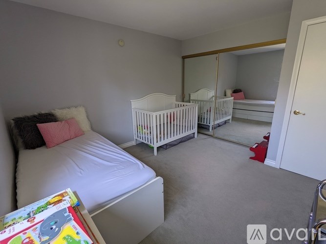 A white crib sits in a room with a white bed and a white dresser.