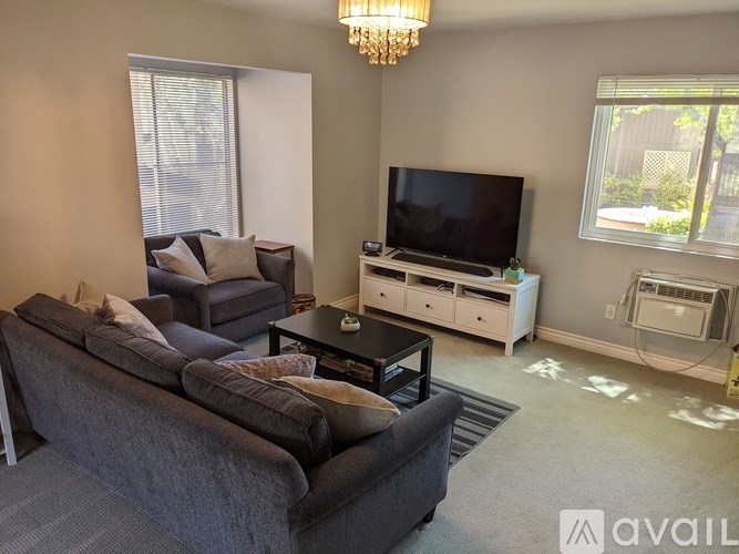 A living room with a grey couch, a black coffee table, a flat screen TV, and a chandelier.