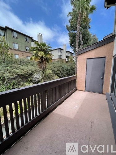 A balcony with a railing and a view of a green hillside with trees and buildings.