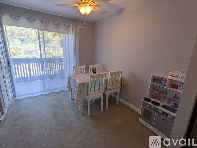 A dining area with a table and chairs is set up in a room with a fan and a window.