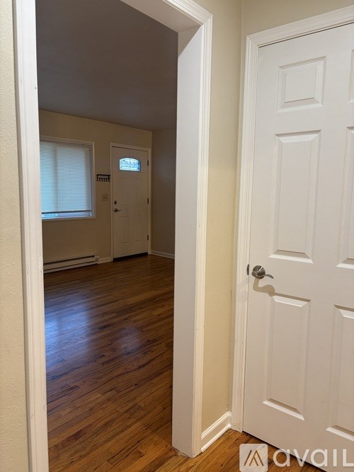 A white door is open to a hallway with wood floors.
