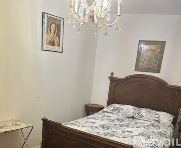 A bedroom with a bed, a chandelier, and two pictures on the wall.