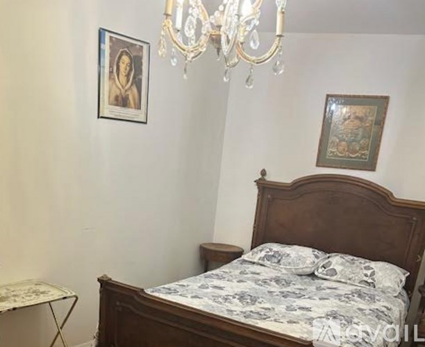 A bedroom with a bed, a chandelier, and two pictures on the wall.