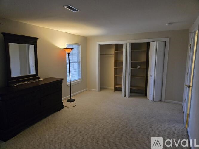 A room with a carpeted floor, a wooden dresser, a mirror, a floor lamp, and a sliding door.
