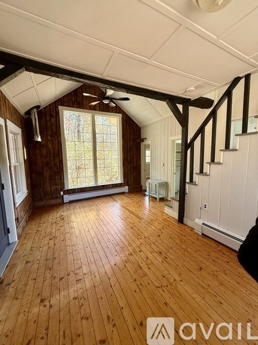 A room with wooden floors and white walls, with a window and a ceiling fan.