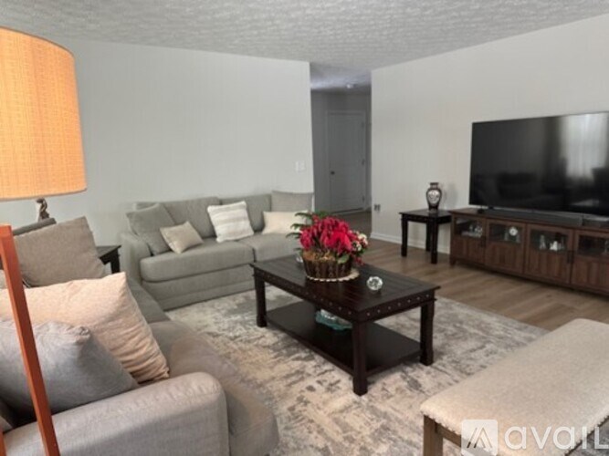 A living room with a grey couch, a coffee table with flowers, and a television.
