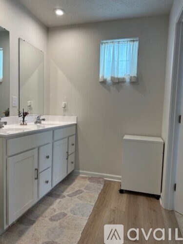 A bathroom with a white cabinet, sink, and a window with white curtains.
