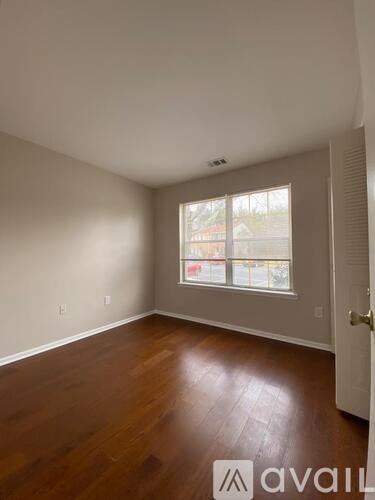 A room with wooden floors and a window showing a view of a fence and trees.