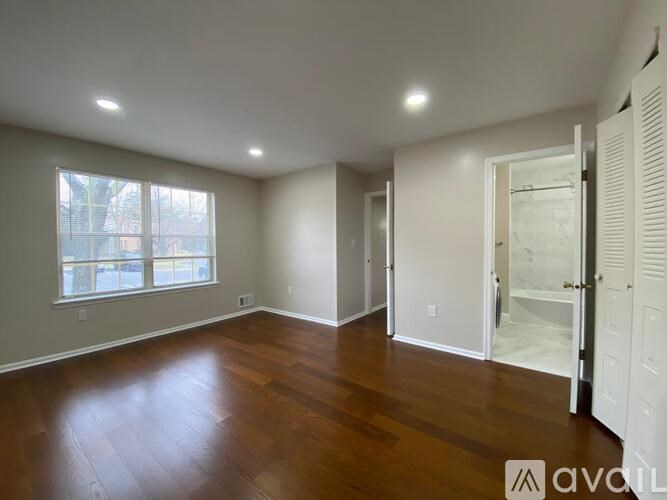 A room with wooden floors and white walls, with a window on the left side.