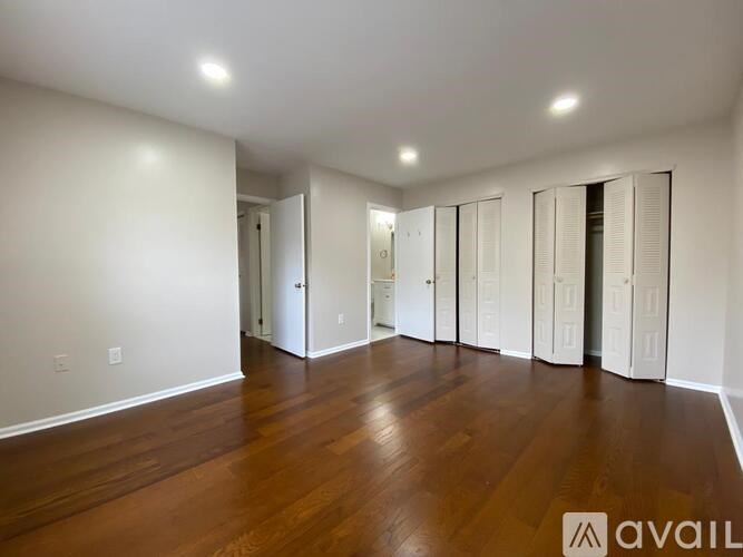 A spacious room with wooden floors and white walls, featuring a row of white closets.