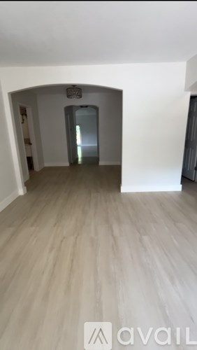 A room with a wooden floor and a white wall with a doorway.