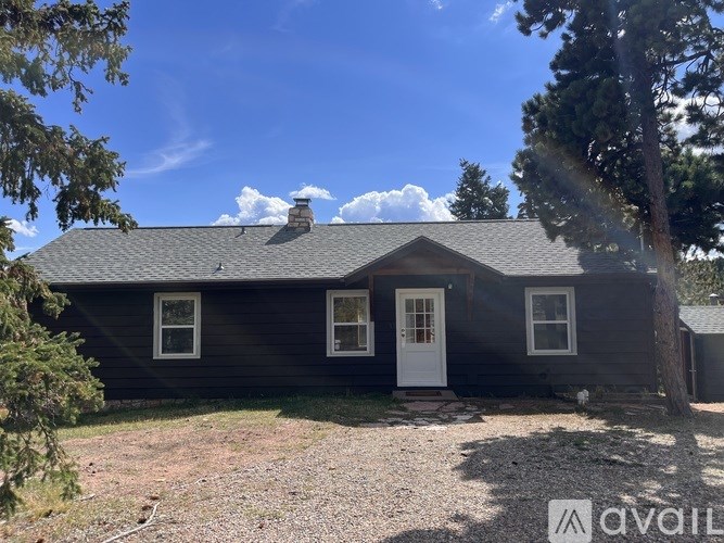 A house with a white door and windows is surrounded by trees.
