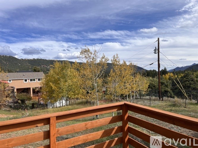 A wooden fence with a sign that reads "AVAIL" in front of a house with trees and mountains in the background.