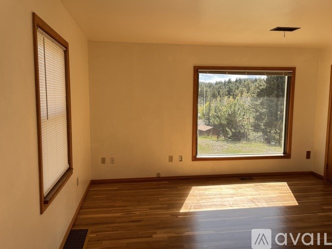 A room with wooden floors and a large window overlooking a forest.