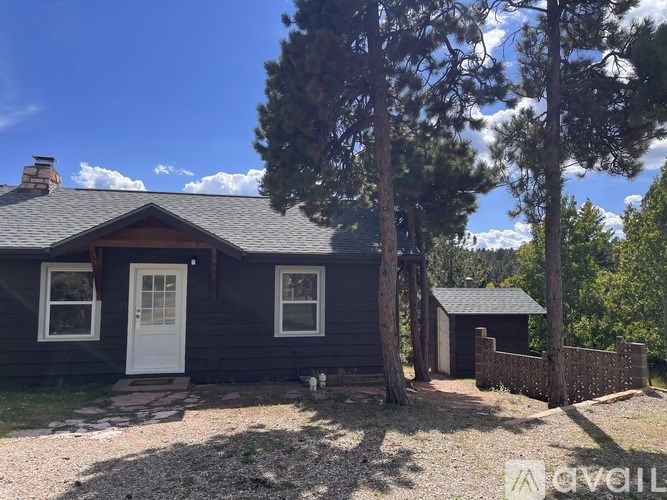 A small house with a white door and windows is surrounded by trees.