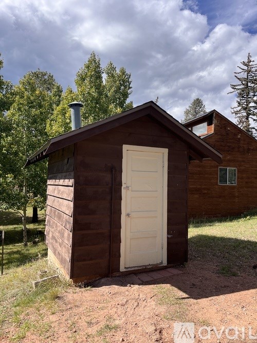 A small wooden building with a white door stands in a field.