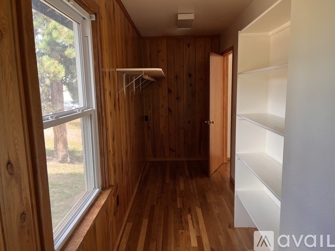 A room with wooden walls and floors, a window, and a white shelf.