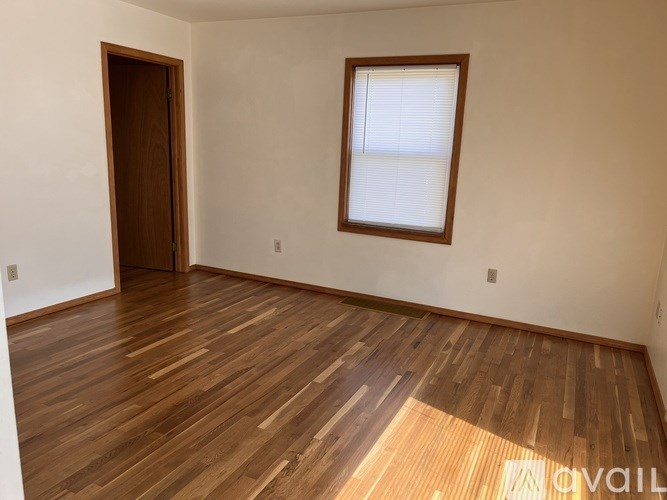 A room with wooden flooring and a window with blinds.