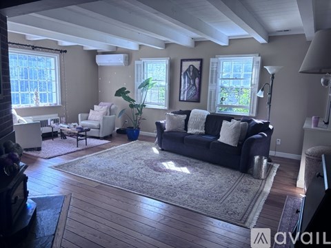 A living room with a black couch and a rug in the center.