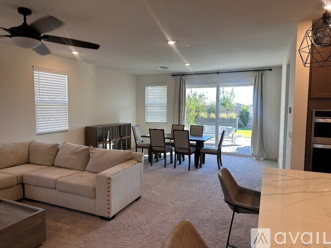 A living room with a white couch, a dining table with chairs, and a ceiling fan.