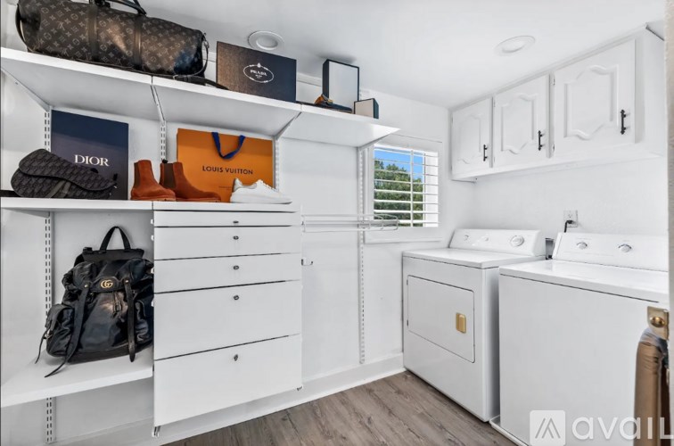 A laundry room with a washer and dryer, a backpack, and a Louis Vuitton bag on the shelves.
