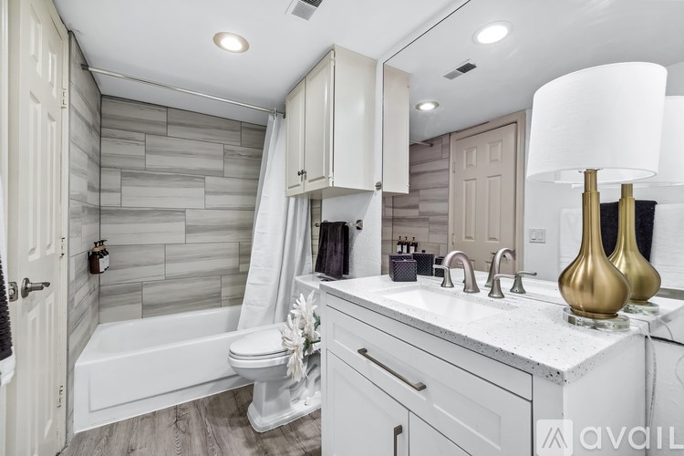A bathroom with a white tub, sink, and a gold vase on the counter.