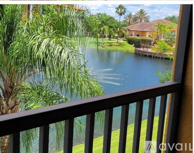 A view from a balcony overlooking a body of water with a house and palm trees in the distance.
