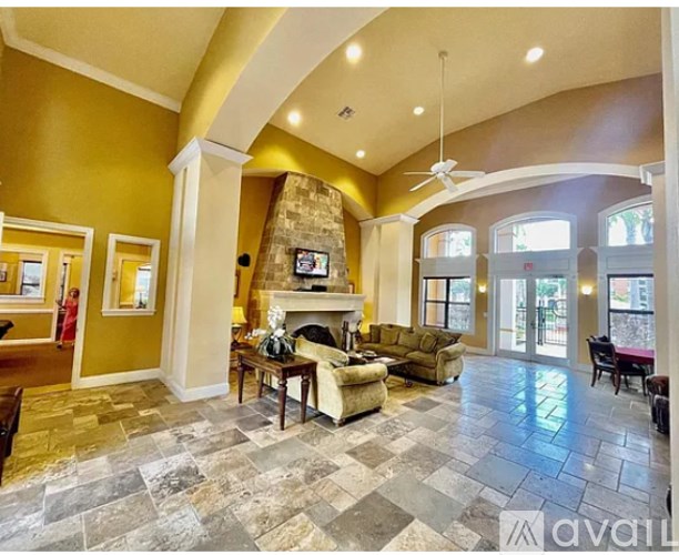 A spacious living room with a stone fireplace and a fan.