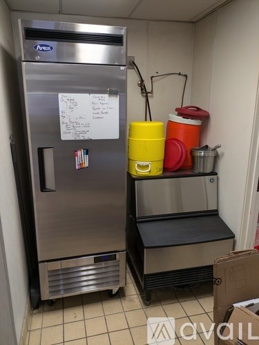 A stainless steel refrigerator with a white paper taped to it and a yellow and red container on the floor.