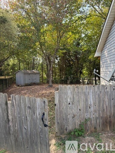 A wooden fence with a gate stands in front of a tree and a shed.