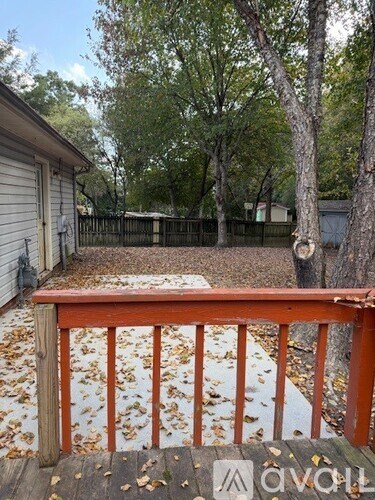 A wooden deck with a railing and fallen leaves on the ground.