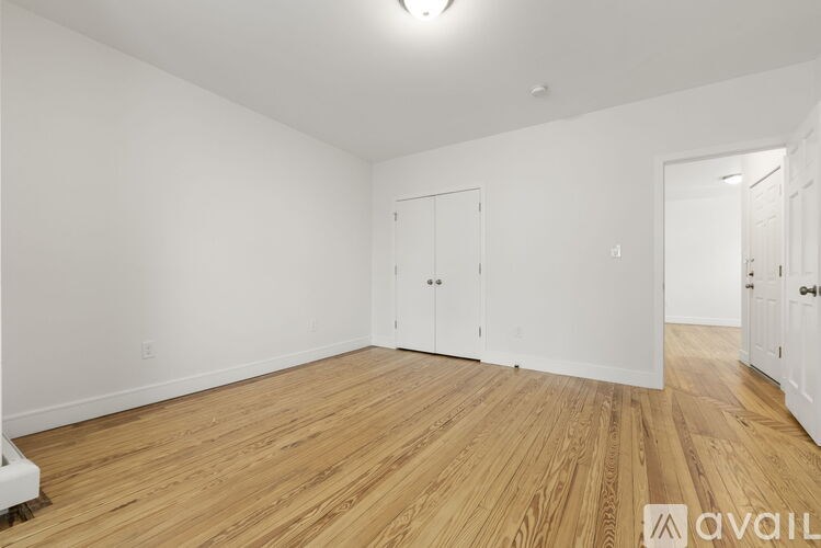 A room with wooden flooring and white walls, with a door on the left and another door on the right.