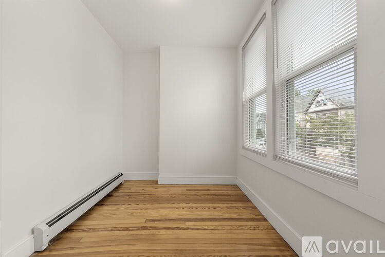A room with wooden floors and white walls with a window and blinds.