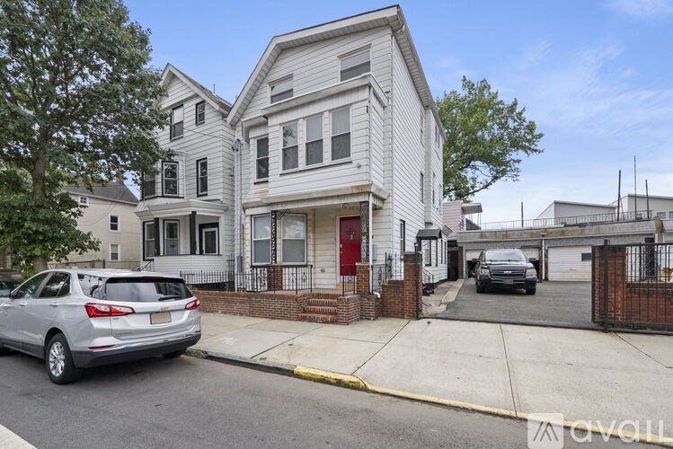 A silver car is parked on the side of a street in front of a white house with a red door.