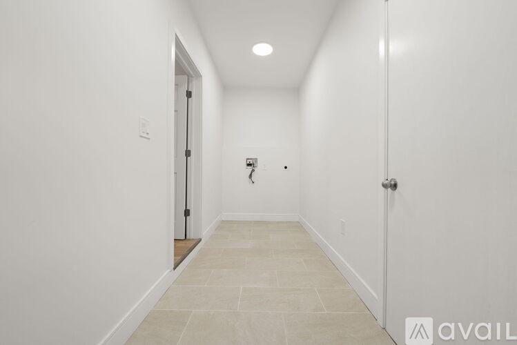 A long hallway with a door on the left and a wall-mounted light fixture on the right.