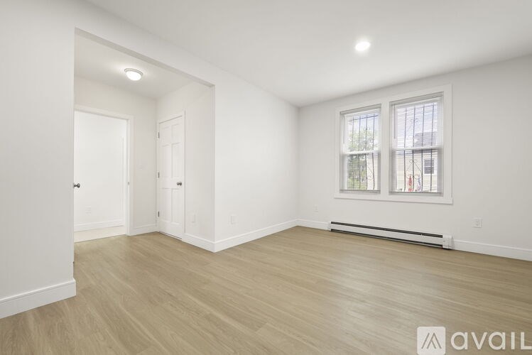 A spacious room with wooden flooring and a window with blinds.
